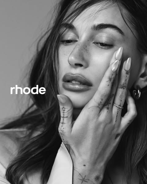 A black and white image promoting Rhode skincare, featuring a close-up of a model, who is also the founder, with her han