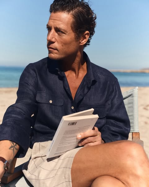 An image ad promoting men's linen clothing, featuring a man sitting outside, reading a book, and wearing a linen shi