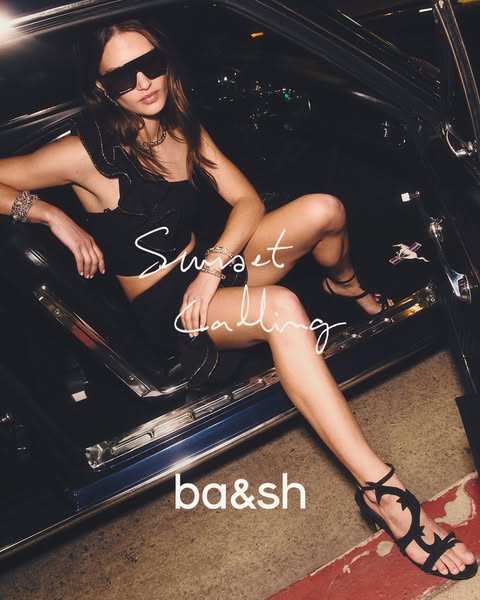 An advertisement for ba&sh apparel. The ad shows a woman in a black outfit and black sandals sitting in the open doo