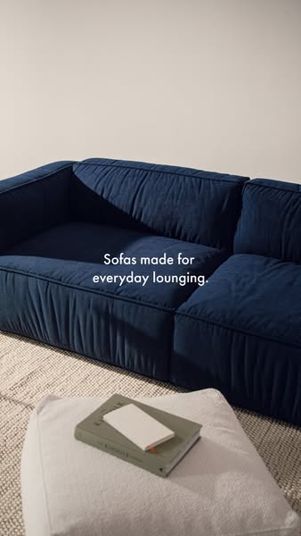 This image ad showcases a navy blue sofa with a book and notebook on a pouf. The ad emphasizes the sofa's comfort an