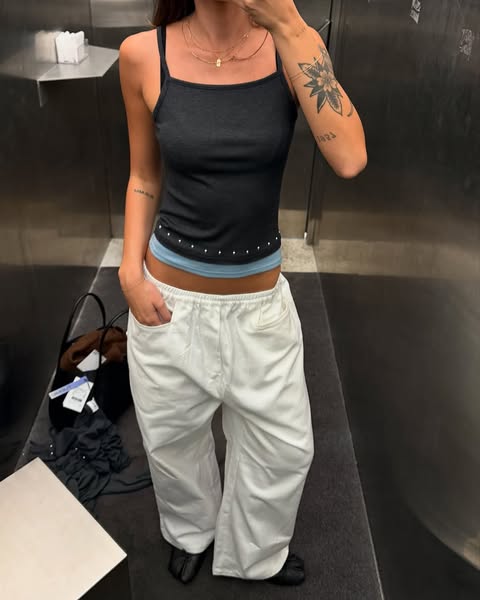 This ad features a woman in a mirror selfie, showcasing a casual outfit of a tank top and white pants. The ad is likely 