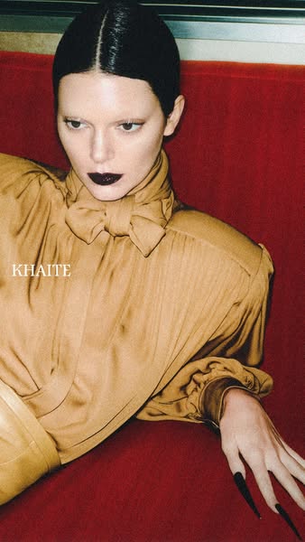 This image ad from Khaite features a woman with stark, neutral makeup wearing a gold-colored blouse. The ad's style 