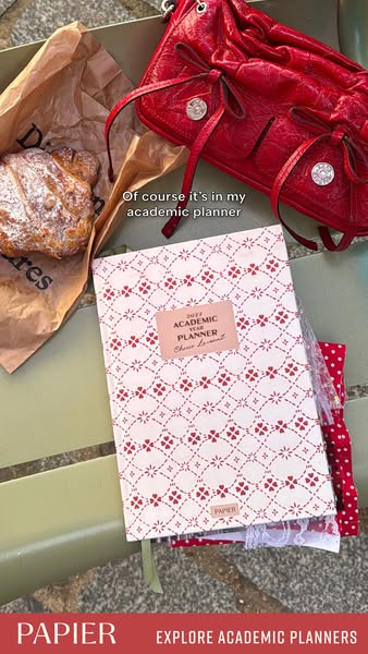 This ad showcases Papier's academic planners in a lifestyle setting with a croissant, red purse, and other academic 