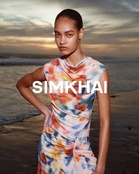 A photo ad for the brand SIMKHAI featuring a model wearing a dress on a beach.