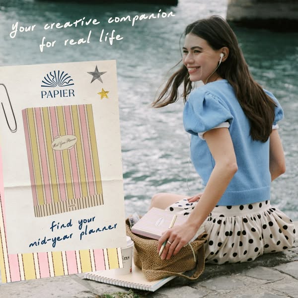 This image ad for Papier shows a young woman next to a body of water using the brand's mid-year planner. The ad is s