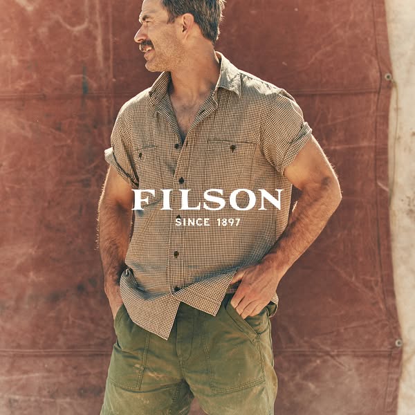 This image ad features a man wearing a Filson shirt and shorts. The Filson logo is prominently displayed in the center o