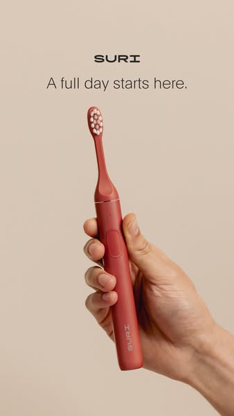This ad features a hand holding the Suri toothbrush against a simple background, highlighting the toothbrush as a stylis