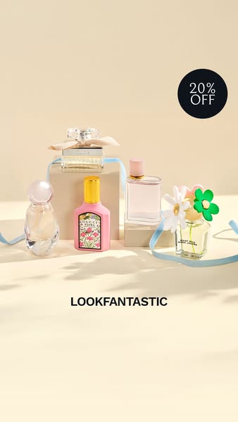 A still-life studio shot features five different bottles of perfume on a light beige surface. A dark blue ribbon and whi