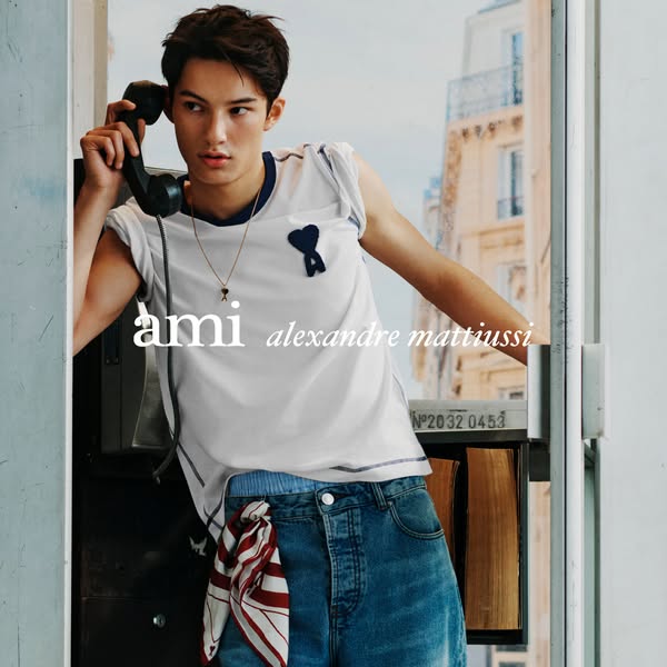 The image is an ad for AMI Alexandre Mattiussi, featuring a man holding a telephone in front of a building.