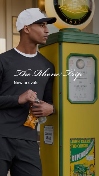 An image ad for Rhone clothing featuring a man in a long-sleeved shirt and athletic cap standing next to a vintage gas p
