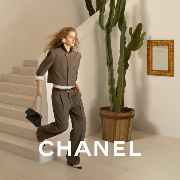 A woman walks down stairs carrying a black Chanel bag. The brand name is emblazoned at the bottom of the image.