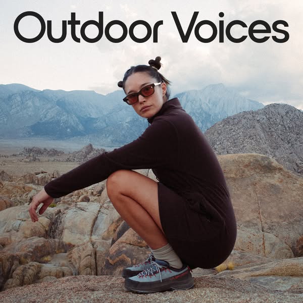 This image ad features a woman in athletic clothing squatting on a rocky surface in front of a mountain range. The ad em