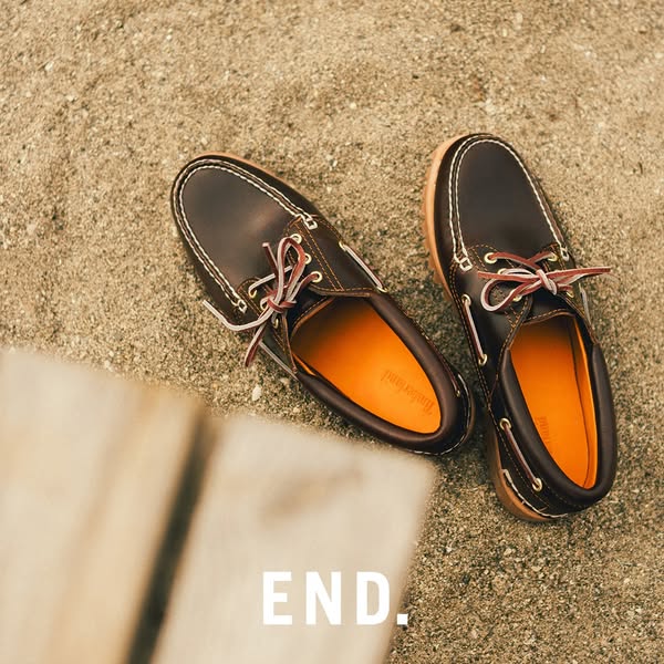 This ad showcases Timberland boat shoes on a sandy surface next to a wooden object, with the word "END." layer