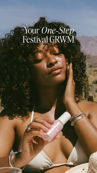 A woman with tan skin, curly hair, and a white bikini top is outside in a desert-like environment. She is holding the pr