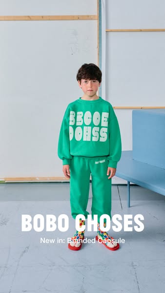 This image ad showcases a young child wearing clothing from Bobo Choses' new Branded Capsule collection. The child i