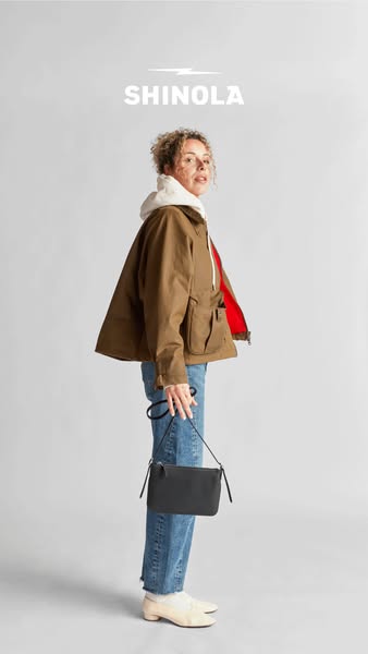 A full shot of a model in a brand jacket and a crossbody bag. The brand logo sits at the top of the image.