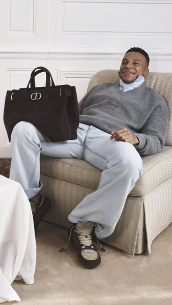 This ad features Kylian Mbappé sitting in a chair with a Dior bag in his lap.