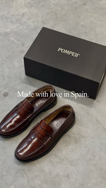 This image ad shows a pair of Pompeii brand brown leather loafers on a concrete surface, next to a black shoebox branded