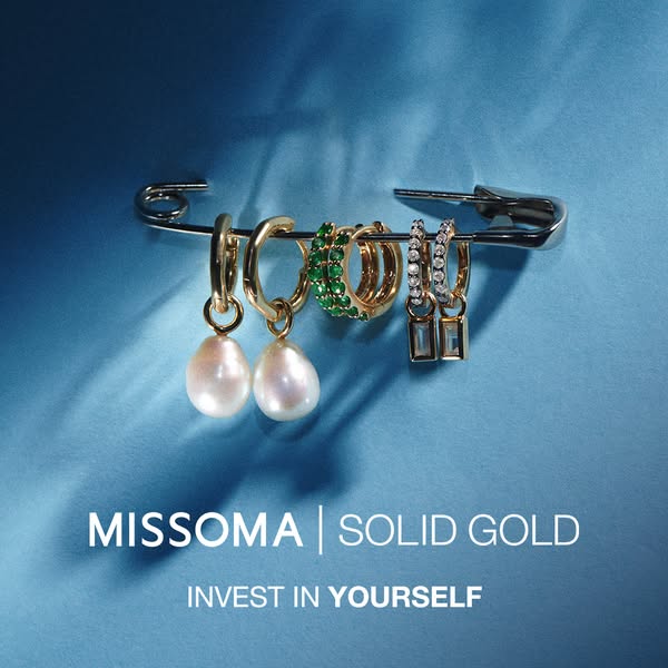This ad showcases Missoma's solid gold earrings, arranged on a safety pin against a blue backdrop, emphasizing the v