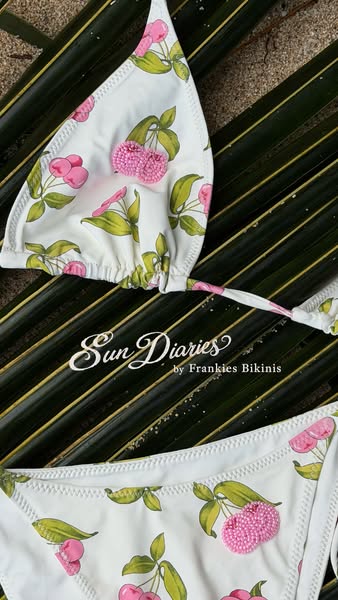 A close-up shot showcases a bikini featuring a white background with a cherry pattern. The brand name 'Sun Diaries b