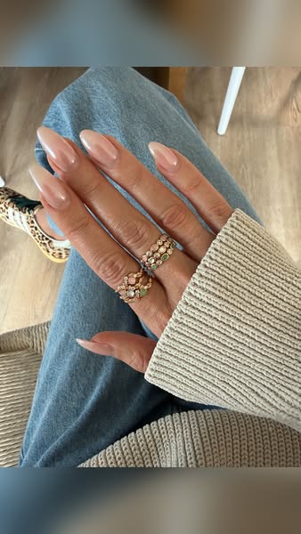 Close-up of someone's hand with a fresh gel manicure. The person is wearing multiple gold rings, light wash jeans, a