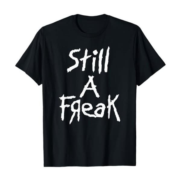 This is a still image ad of a black t-shirt that has the words, "Still a Freak" on it in white letters. The ad