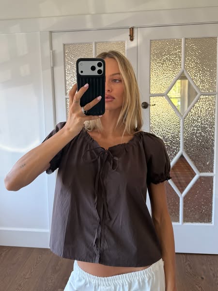 This ad features a woman wearing a brown, tie-front blouse. She is holding her phone up to take a selfie.