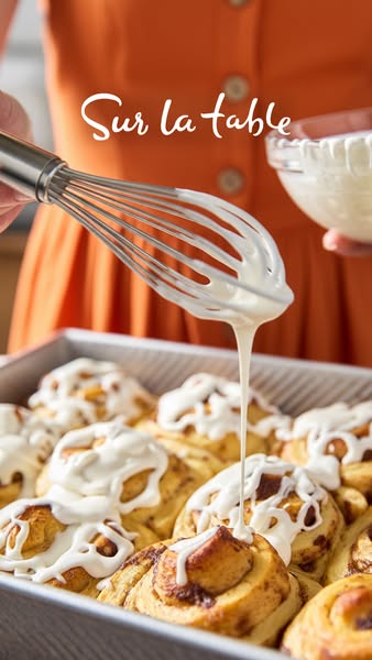 This image is an extreme closeup showing a person icing cinnamon rolls. It may be targeted toward people who enjoy cooki