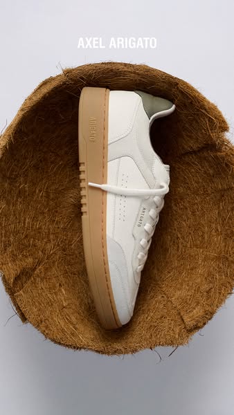 This ad features a single white Axel Arigato sneaker placed inside a hollowed-out coconut shell. The camera angle is str