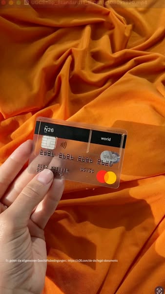 This ad showcases a transparent N26 debit card against an orange fabric background. The card is displayed and slightly m