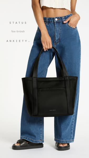 This ad promotes a black Status Anxiety tote bag, showcasing it as part of a stylish, casual outfit. The ad focuses on n