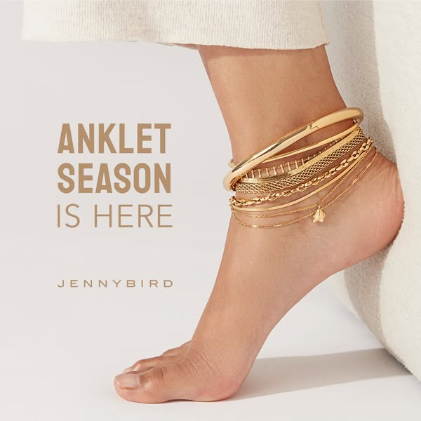 This image ad promotes Jenny Bird anklets. The image features a foot adorned with multiple gold anklets, emphasizing a s