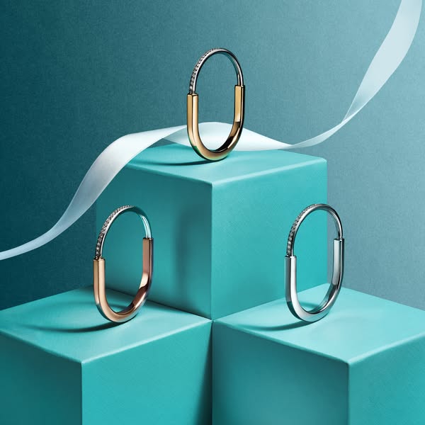 A still life image ad featuring three versions of the Tiffany Lock bangle on turquoise geometric risers. The ad is highl