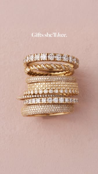 This ad showcases a stack of gold and diamond rings against a solid pink background, with the headline 'Gifts she
