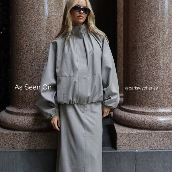 This ad features a photograph of a woman standing in front of columns wearing a matching grey skirt and jacket. The ad i