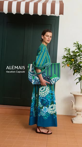A woman stands outdoors in front of a green door with an awning above. She's wearing a matching outfit and holding a