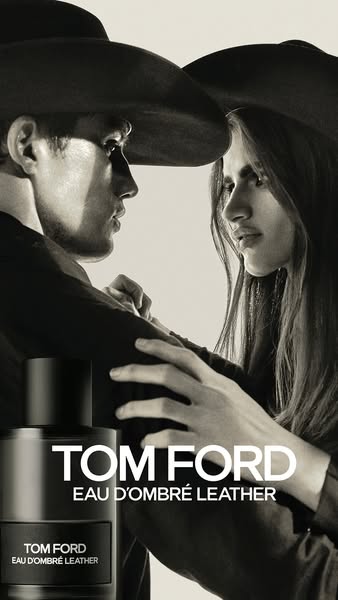 This is an image ad for TOM FORD Eau d'Ombré Leather. The image features a man and woman in cowboy hats standing clo