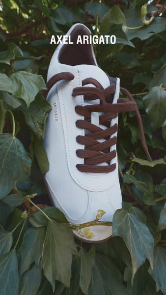 This image ad showcases a white Axel Arigato shoe surrounded by green leaves.