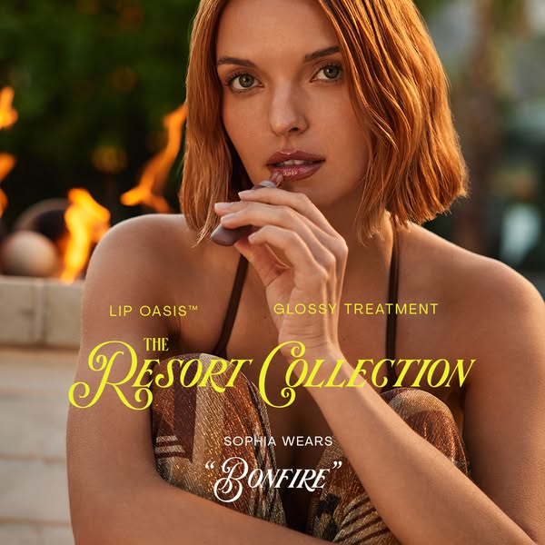 A beauty brand is promoting its glossy lip treatment through a lifestyle shot of a model applying the product in a warm,