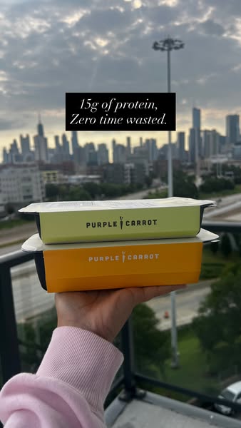 This image ad features a person holding two Purple Carrot prepared meal containers in front of a city skyline to highlig