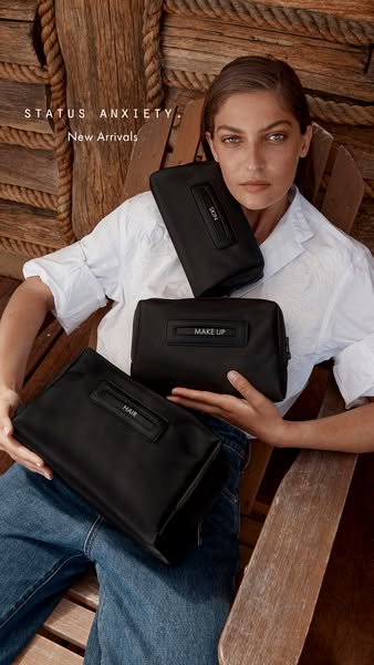 This ad features a woman sitting in a wooden chair holding three Status Anxiety cosmetic bags. The ad copy highlights th