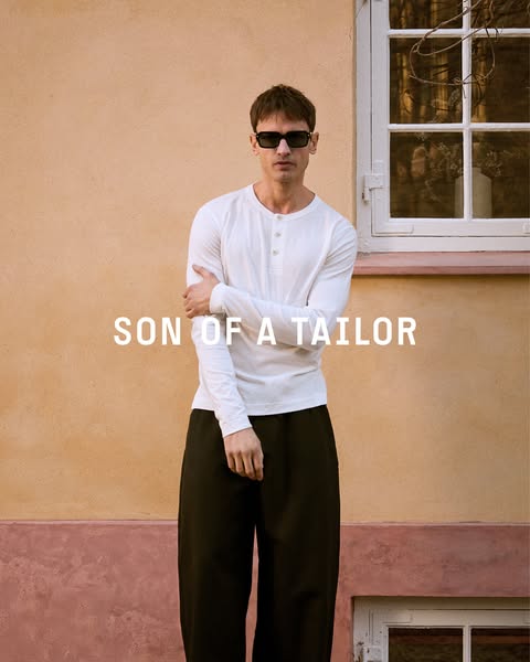This ad for Son of a Tailor features a man wearing a long sleeve shirt and dark pants in front of a light orange wall an