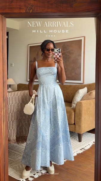 A woman stands in front of a mirror and takes a picture of herself while wearing a light blue patterned dress from Hill 