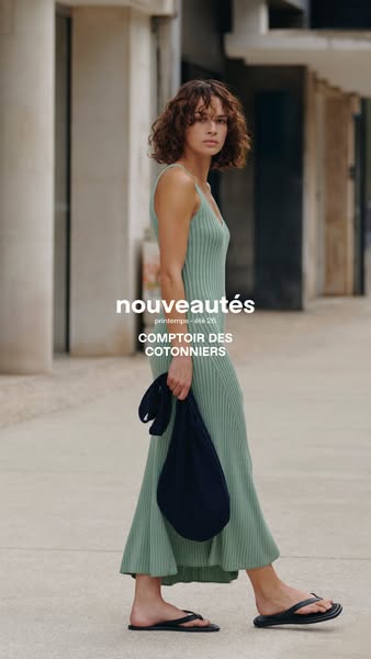 A woman in a seafoam green dress and black flip-flops walks across the screen, holding a navy blue bag in her hand. Text