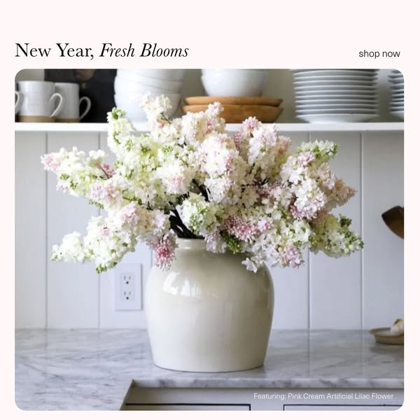 This ad showcases pink and white artificial lilac flowers in a neutral-colored vase set in a neutral kitchen setting. It