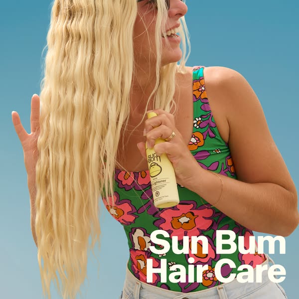 A summery ad features a blonde woman on a sunny day holding a bottle of Sun Bum hair lightener and smiling.