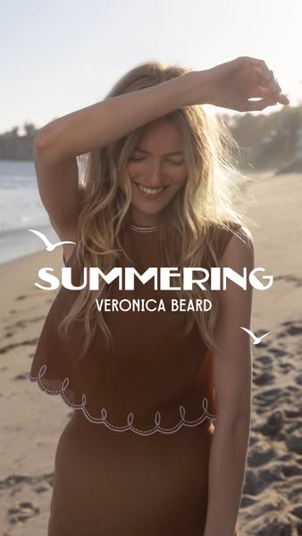 This image ad showcases the Veronica Beard brand. It features a woman standing on a beach, wearing clothing by Veronica 