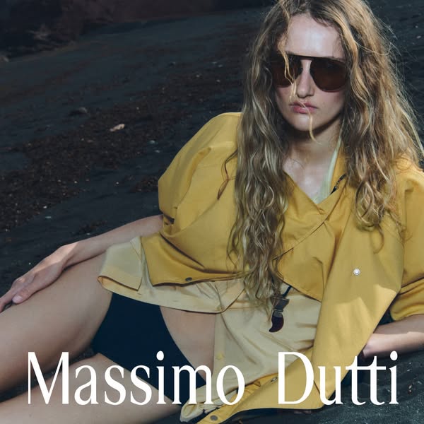 This image ad features a model laying on a beach with dark sand, wearing clothing from Massimo Dutti. The brand's na