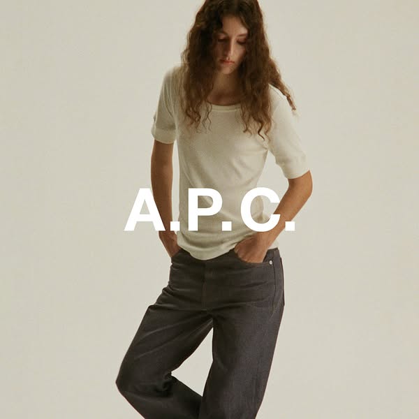 This ad showcases A.P.C. brand clothing. A woman is shown wearing a white top and black pants. The ad is simple, with th