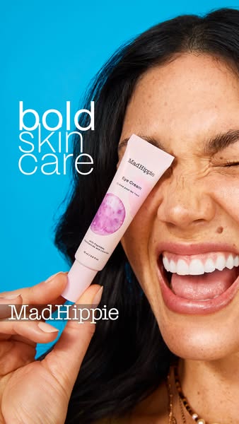 A close up shot of a woman holding Mad Hippie Eye Cream tube to her eye.
